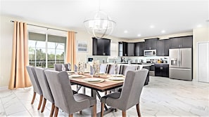 A modern kitchen with dark cabinets, stainless steel appliances, and a dining area with a wooden table and grey chairs. - Magical Family Stay: Pool, Game Room & Disney (Davenport)