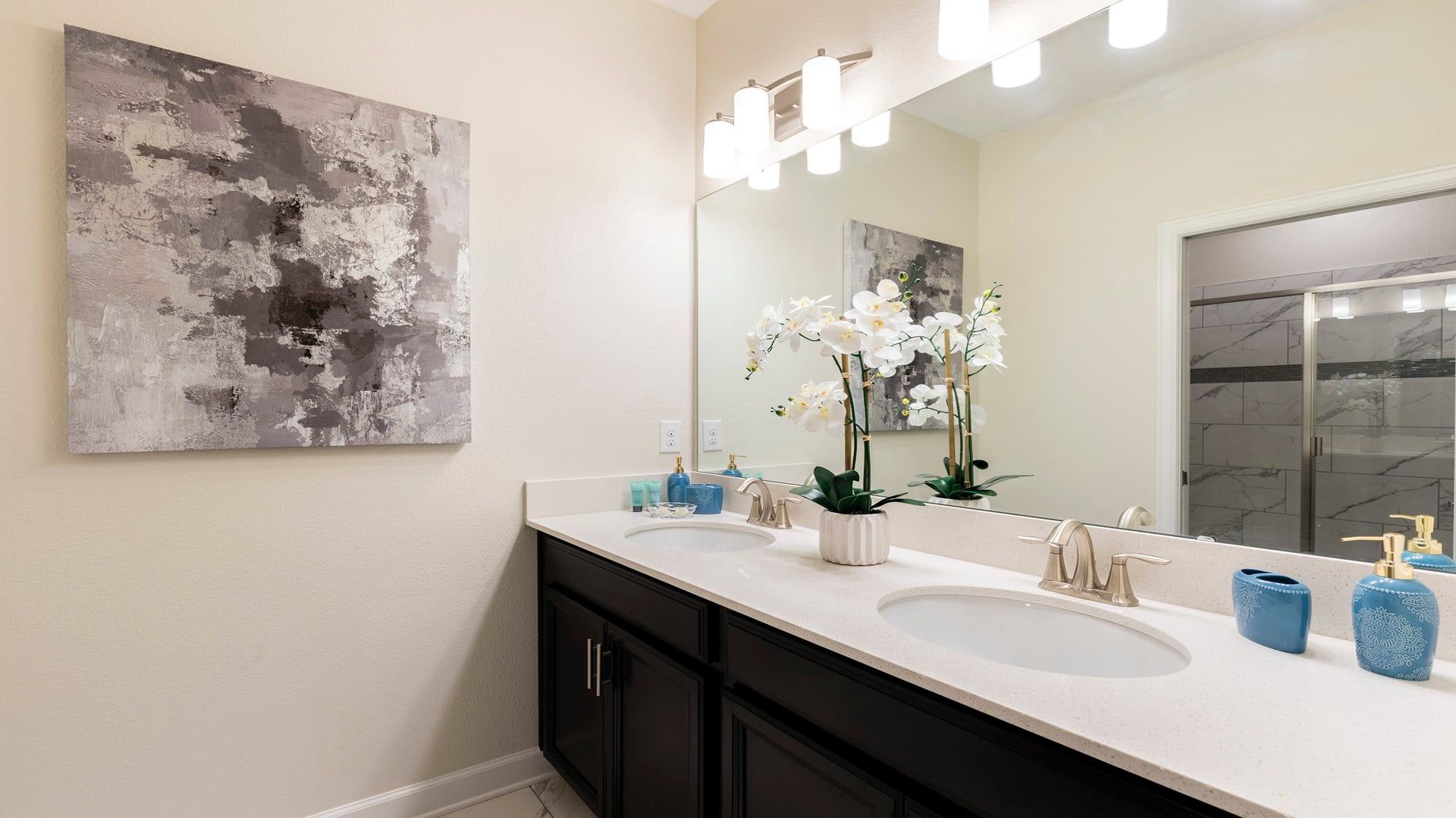 Une salle de bain avec deux lavabos, un grand miroir et un tableau abstrait contemporain.