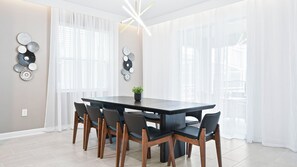 A modern dining area with a dark wooden table, six chairs, and decorative wall art. - Luxe Home w/ Ps5, Pool, & Themed Rooms Near Disney (Kissimmee)