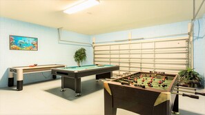 Ein Zimmer mit Poolbillardtisch, Kicker und einem Gemälde an der Wand.