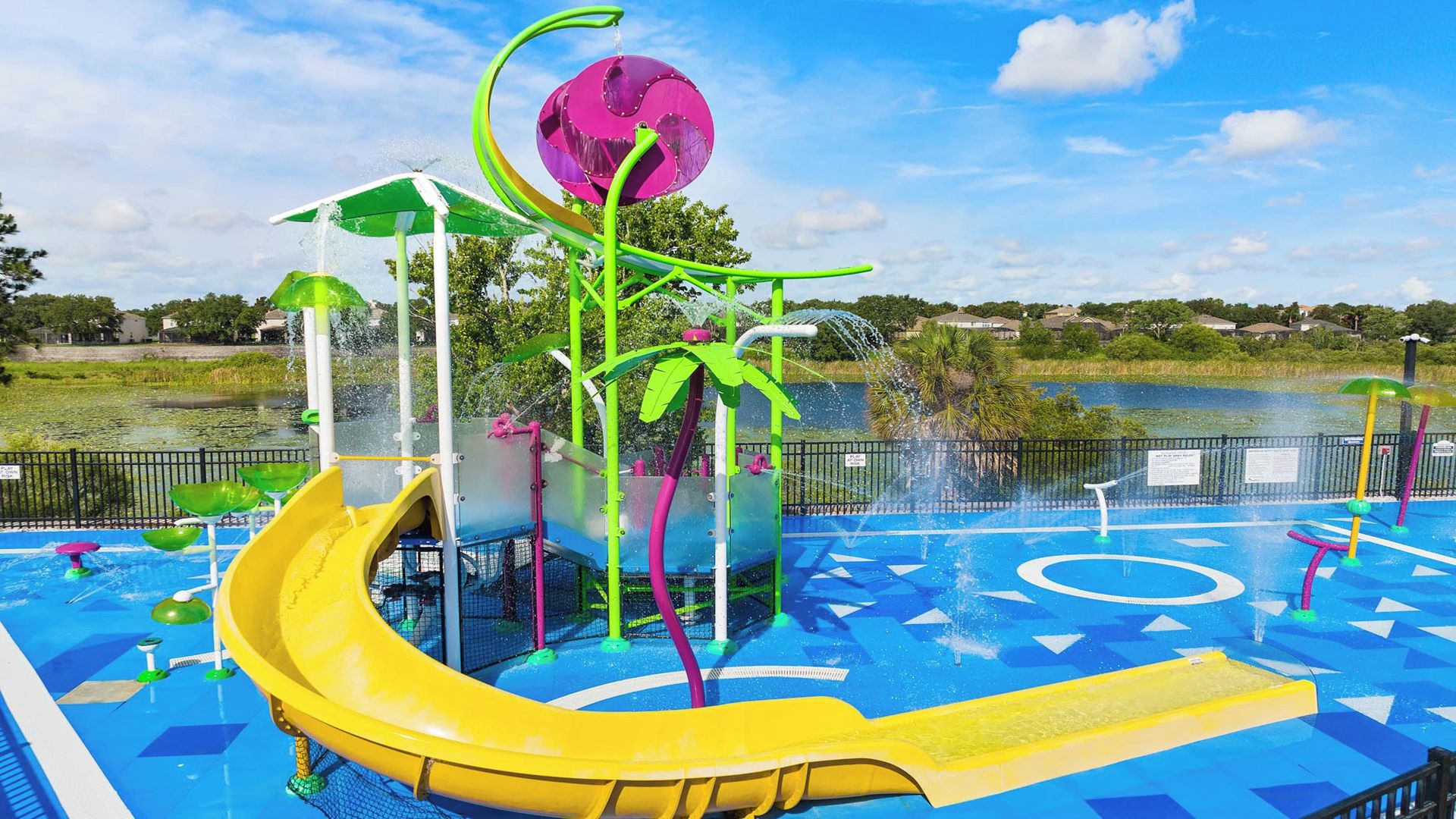 A water park with a yellow slide, a water fountain, and a pool area.