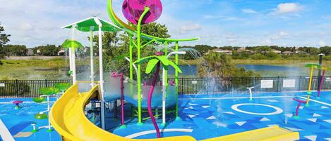 A water park with a yellow slide, a water fountain, and a pool area.