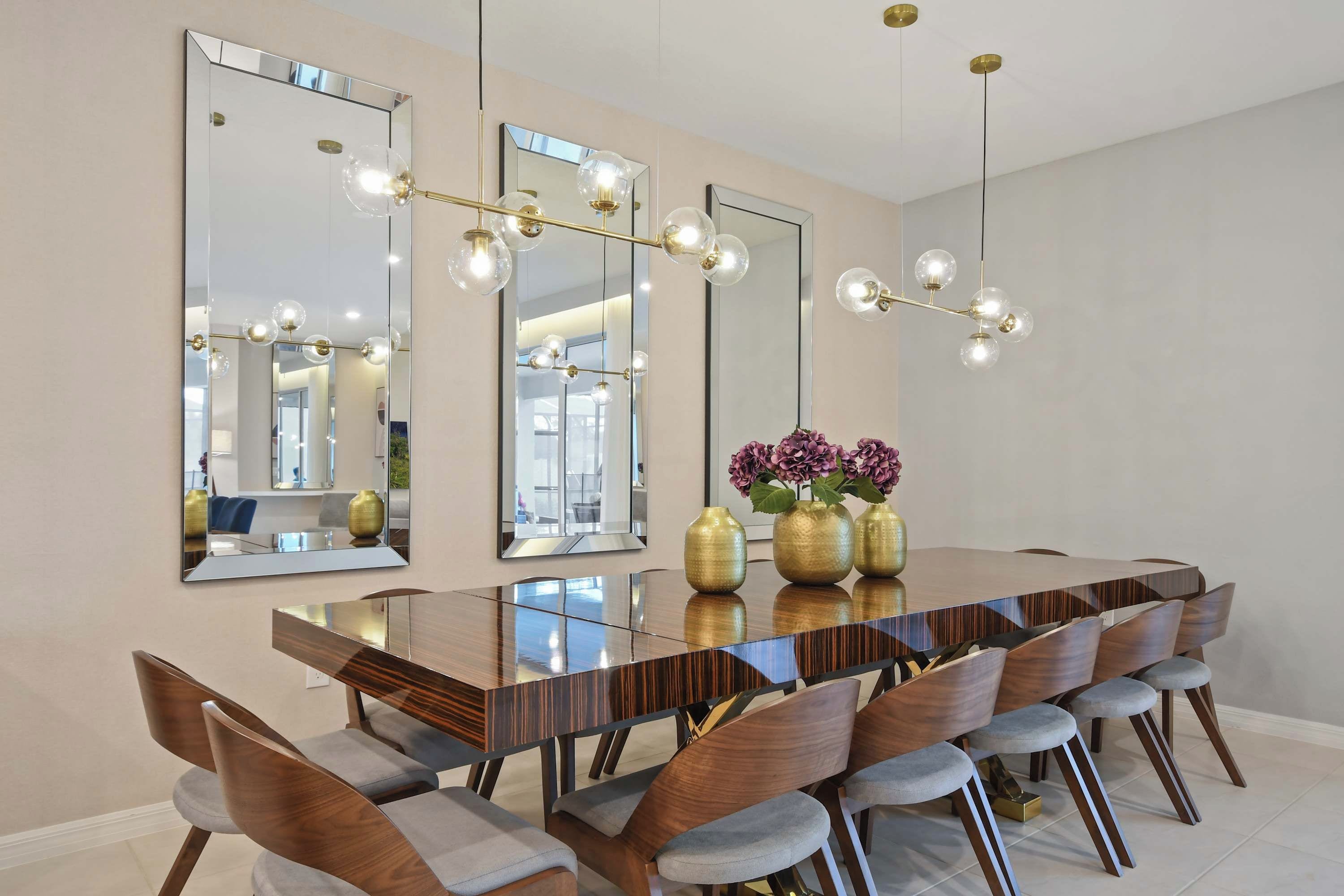 Un espace repas avec une longue table en bois, de nombreuses chaises et de grands miroirs accrochés aux murs.