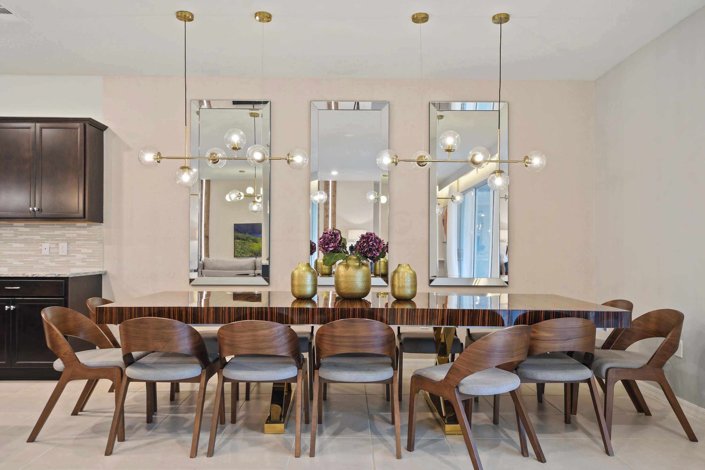 A modern dining area with a long table, six chairs, and three large mirrors.