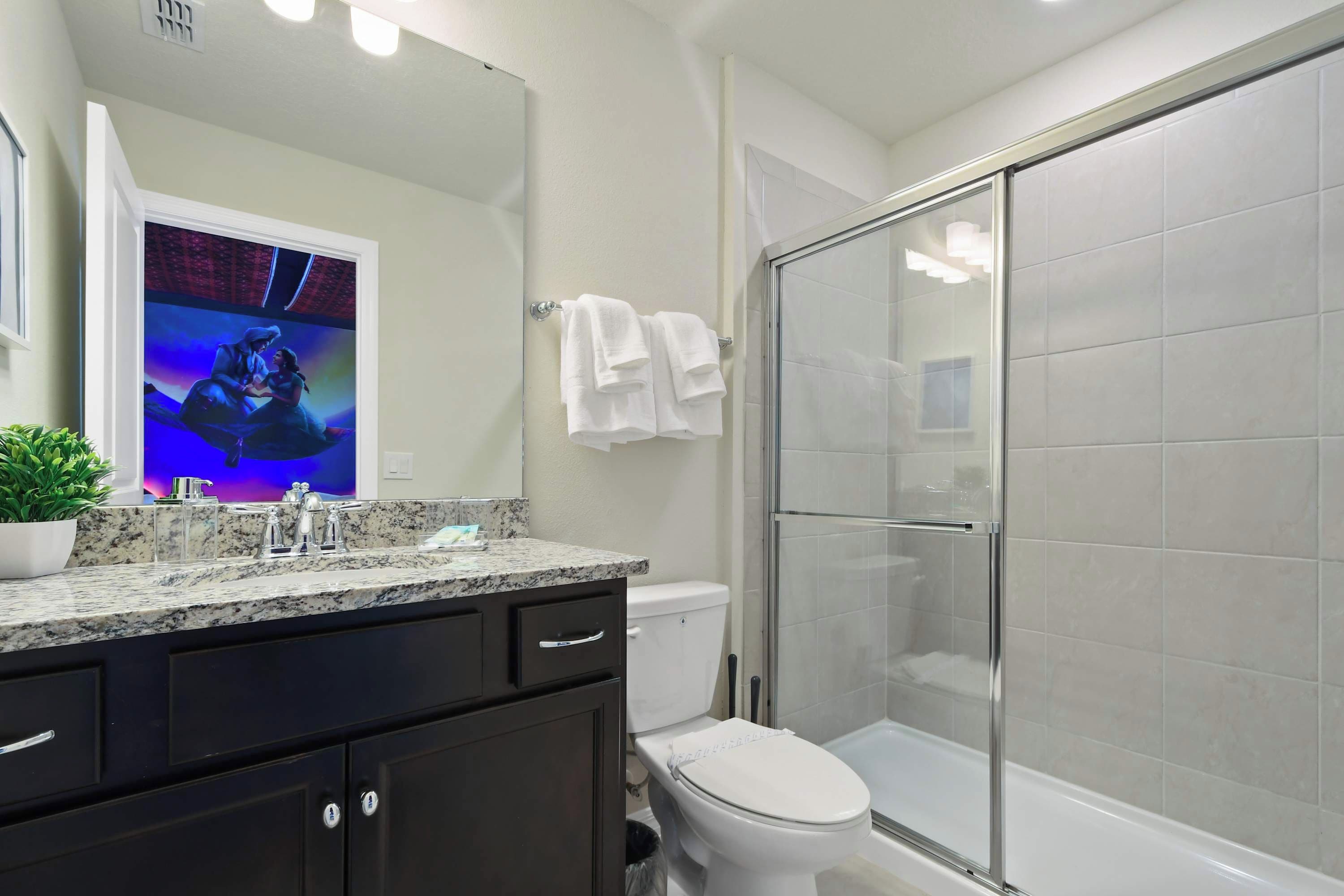A modern bathroom with a granite countertop, dark cabinets, a white toilet, and a glass-enclosed shower.