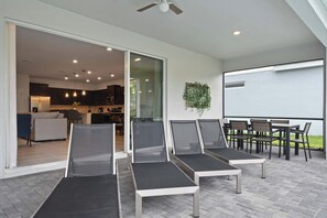 A modern outdoor seating area with lounge chairs and a table, connected to a kitchen and living space. - 10br Windsor Epic Themed Villa Private Pool (Davenport)