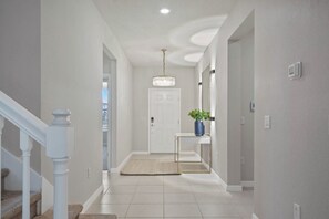 A hallway with a white door, a small table with a plant, and a chandelier. - 10br Windsor Epic Themed Villa Private Pool (Davenport)