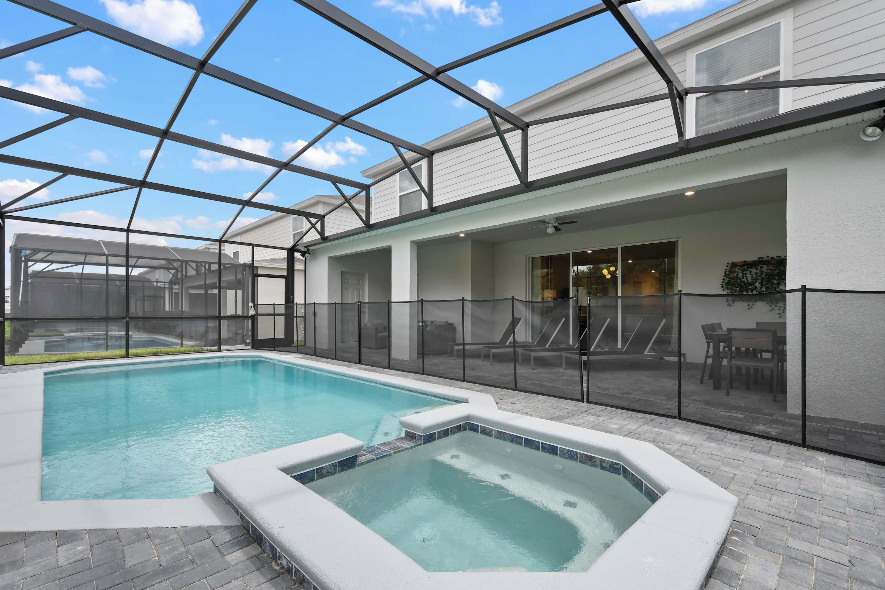 Una piscina exterior techada con un jacuzzi, rodeada por un patio con sillas y una mesa.