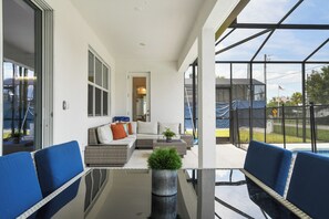 A modern patio with a glass table, blue chairs, and a wicker sofa with cushions. - Nice 15br Home Near Disney Groups Welcome (Kissimmee)
