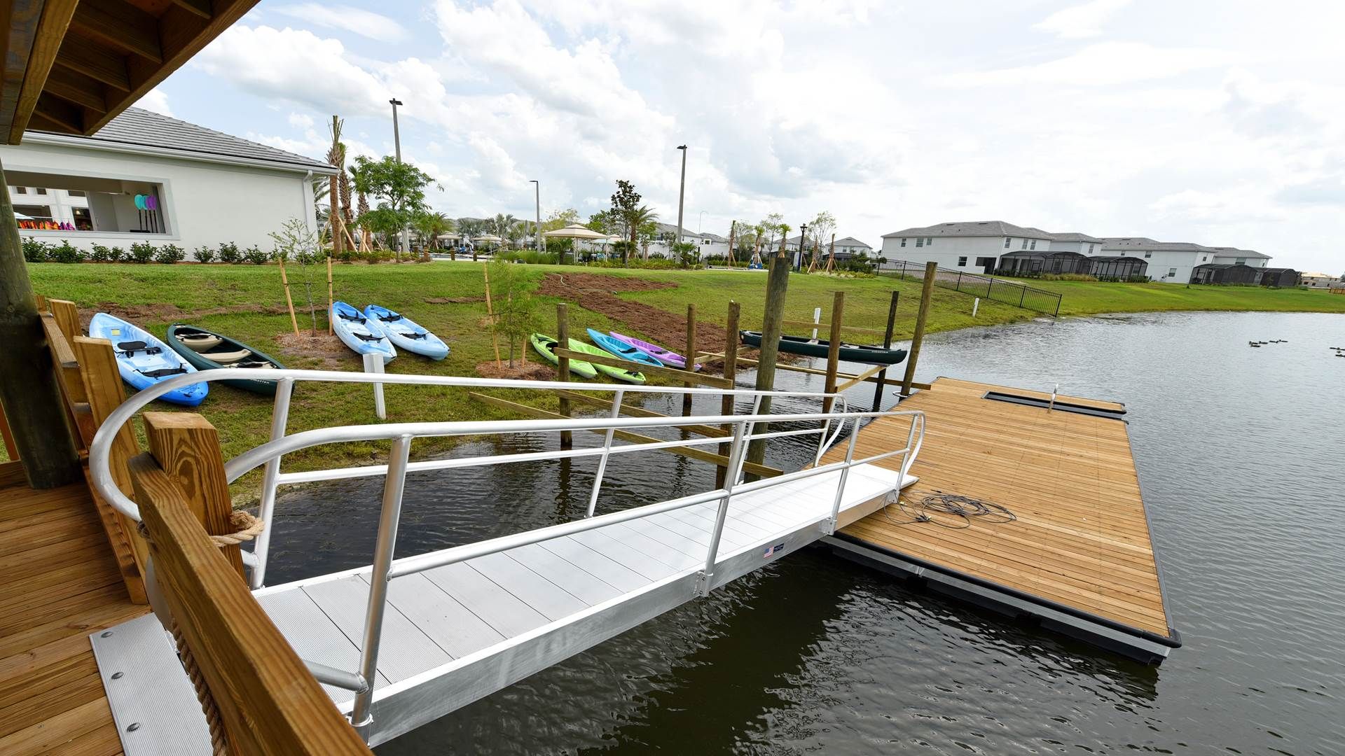 Un muelle de madera se extiende sobre una superficie de agua tranquila, con kayaks y canoas amarrados al otro lado.