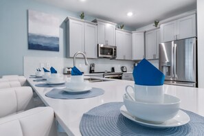 Eine moderne Küche mit weißen Schränken, Edelstahlgeräten und einem Essbereich mit weißen Stühlen und einer blauen Tischmatte.