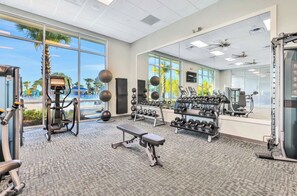A well-lit gym with various exercise equipment, large windows, and a view of palm trees. - New! Avatar Game Room & Harry Potter Fantasy World (Davenport)