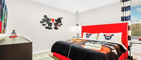 Un dormitorio con cabecera roja, cama con ropa de cama temática de Mickey Mouse y decoración de pared con Mickey y Minnie Mouse.