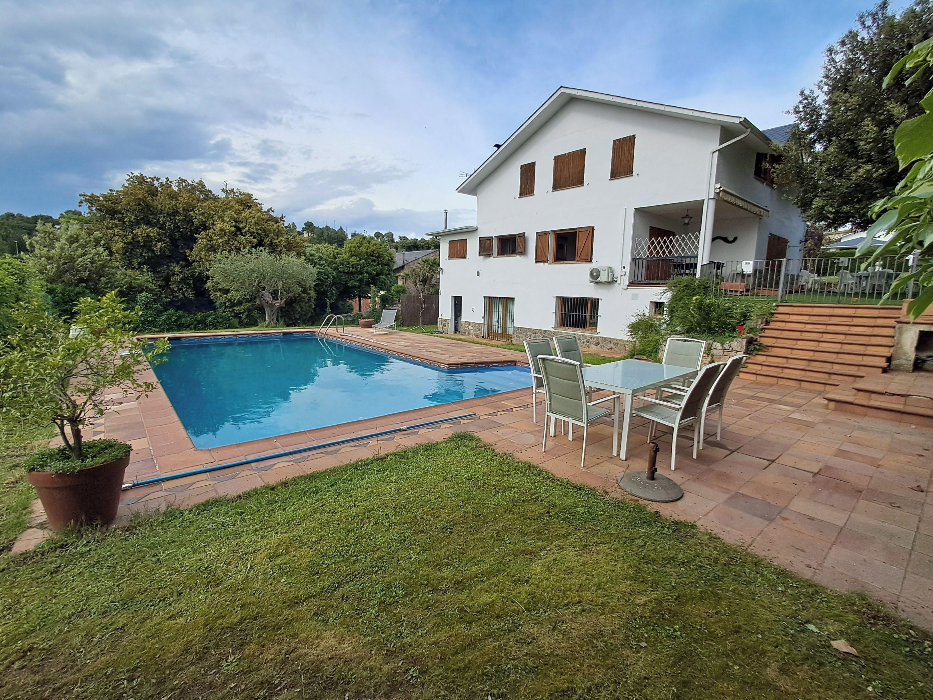 A residential property with a swimming pool, a patio with outdoor furniture, and a white house with multiple windows.