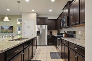 A modern kitchen with dark wood cabinets, stainless steel appliances, granite countertops, and pendant lighting. - Cozy 5BR Townhome w/ Mickey Themed & Pool (Kissimmee)