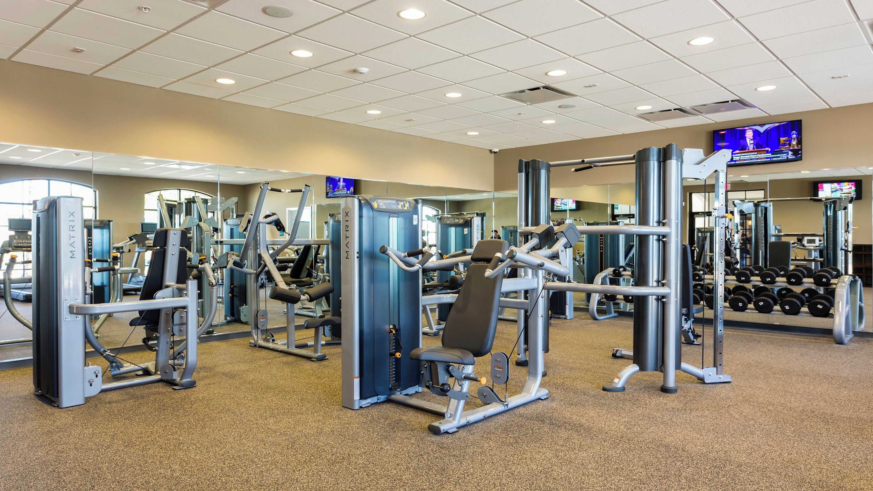 A gym with various exercise machines, mirrors, and a television screen.