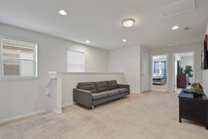 A spacious living room with a grey sofa, a dark wooden coffee table, and a carpeted floor. - Cozy 5BR Townhome w/ Mickey Themed & Pool (Kissimmee)