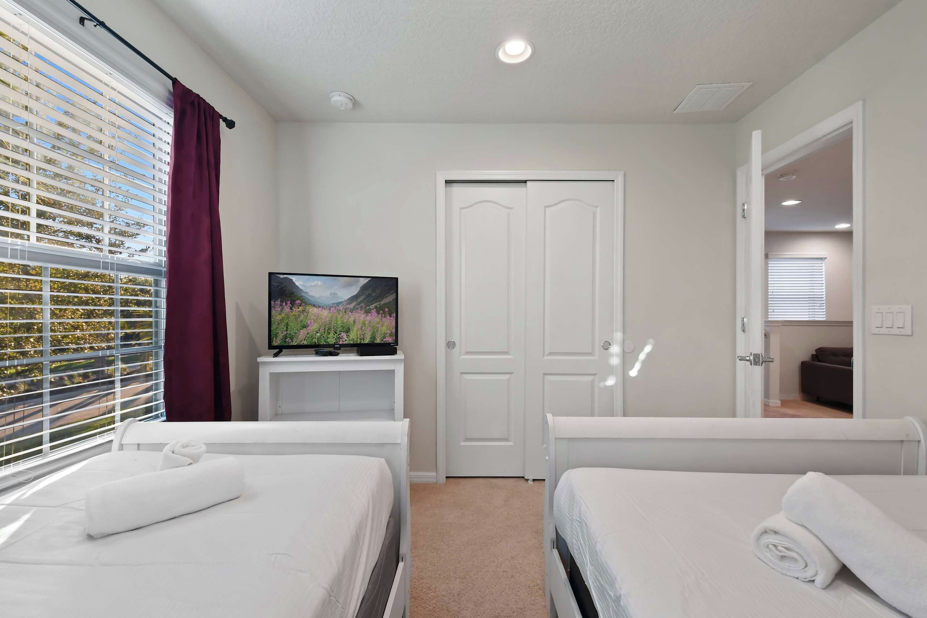 A hotel room with two beds, a television on a stand, a door, and a window with blinds.