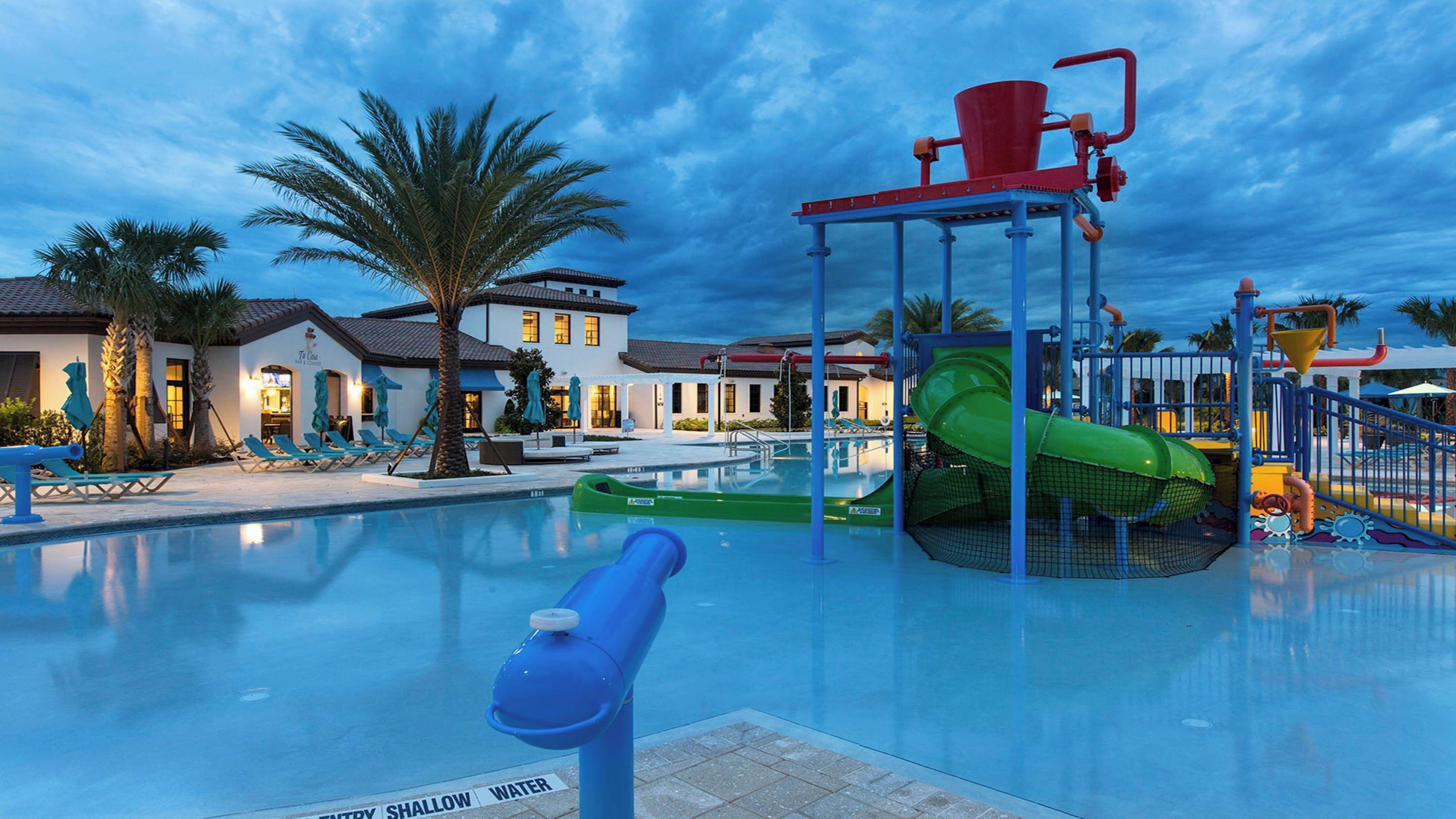 Una piscina con tobogán de agua, sillas de descanso y una palmera.