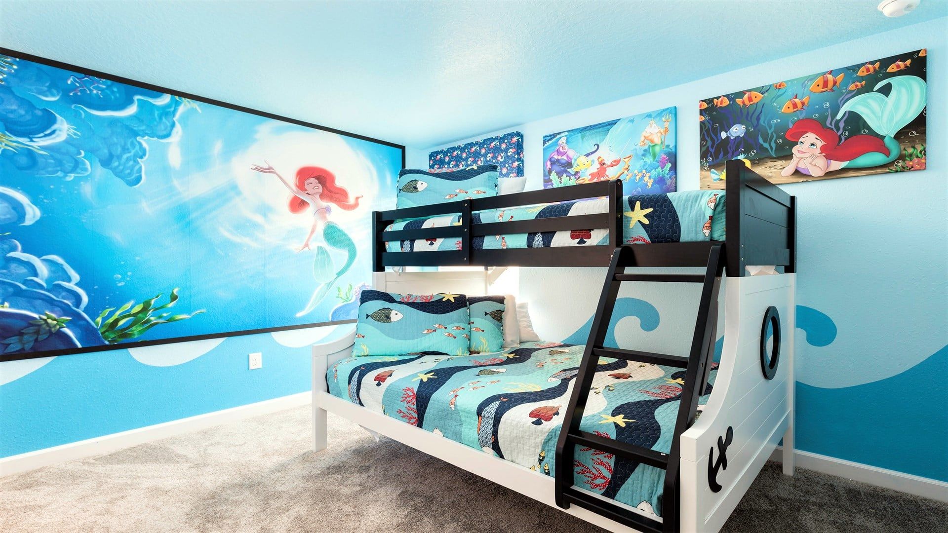 Un lit superposé pour enfant, avec une couverture de lit sur le thème des sirènes, une fresque murale représentant une sirène et une fenêtre donnant sur le ciel.