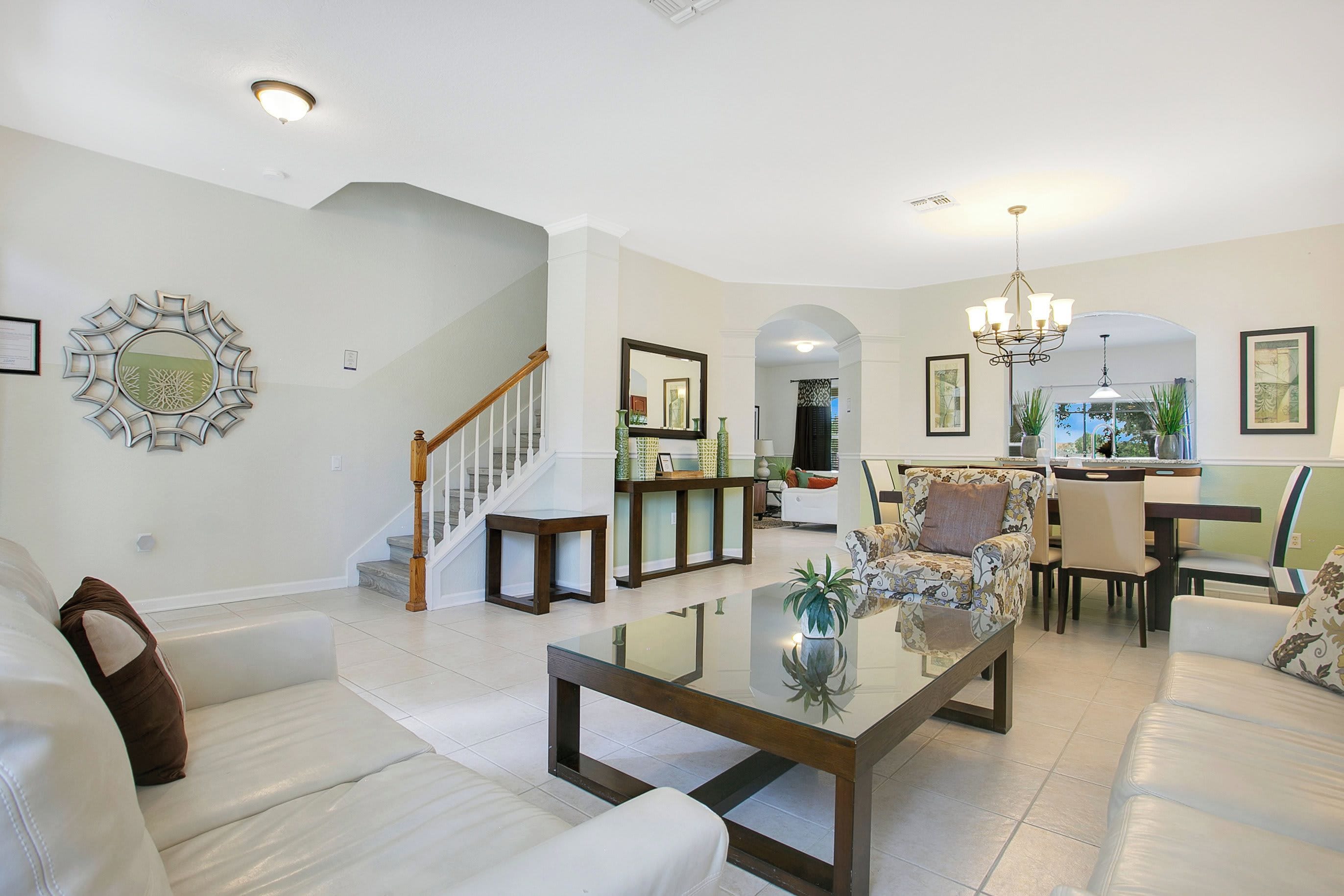 Un salón amplio con una mesa de centro de cristal, una escalera y un comedor con sillas y una araña.