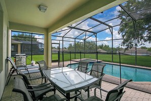 An outdoor patio with a glass table and chairs, a barbecue grill, and a view of a swimming pool and neighborhood houses. - 6BR Disney Villa w/ Pool/spa/game in Windsor Hills (Kissimmee)
