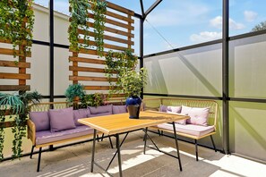 An outdoor patio with a wooden table and two sofas, surrounded by greenery and a glass enclosure. - Star Wars & Jurassic Park Fun Near Disney (Kissimmee)