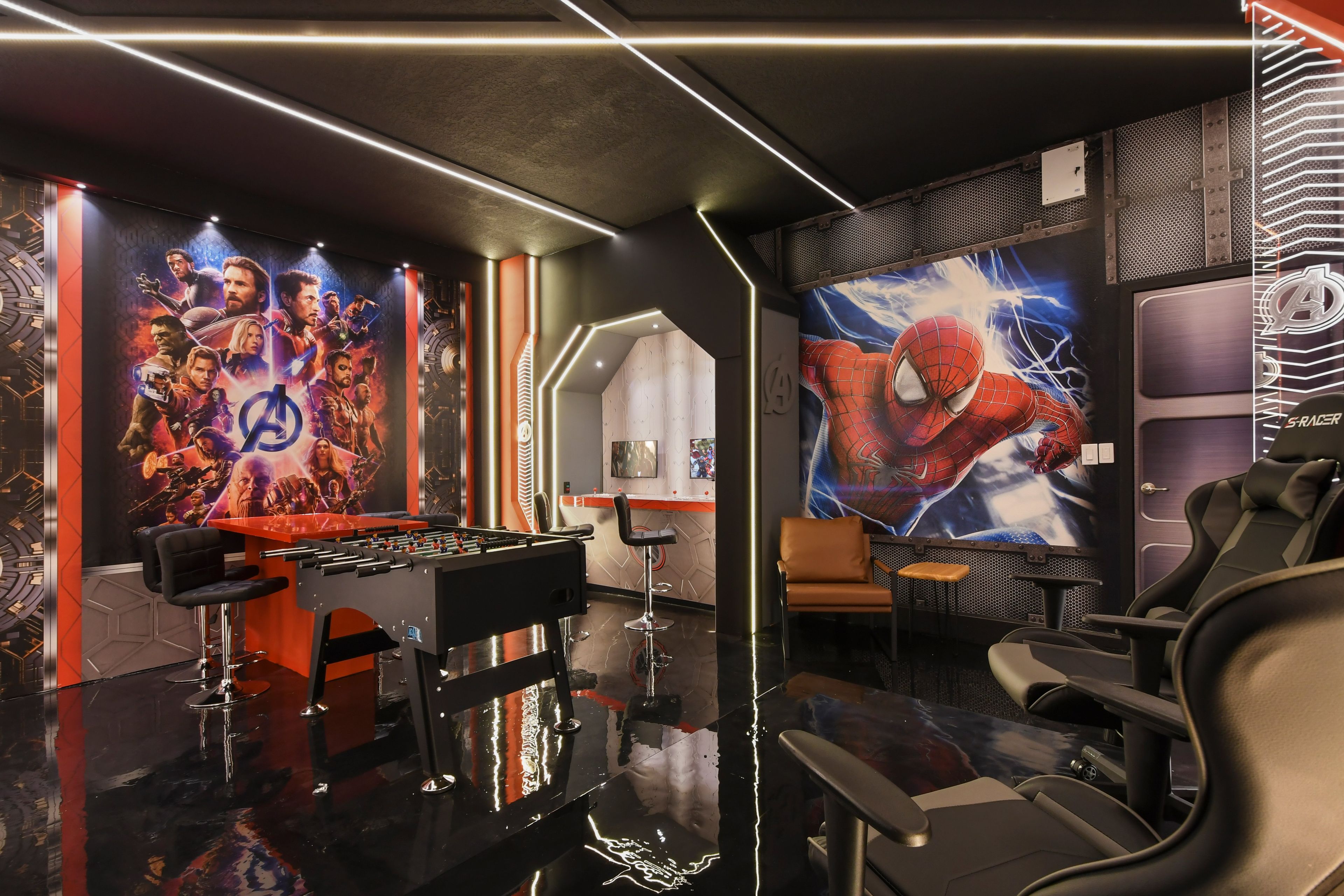 A gaming room with a foosball table, comfortable seating, and large posters of superhero characters.