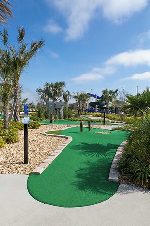 A miniature golf course with a green putting surface, palm trees, and a water slide in the background. - Lakeview Villa Epic Game Room & Pool (Kissimmee)