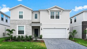 A two-story residential building with a stone facade, a garage, and a well-maintained lawn. - Massive 10br Villa! Themed Bunks & Waterpark (Davenport)