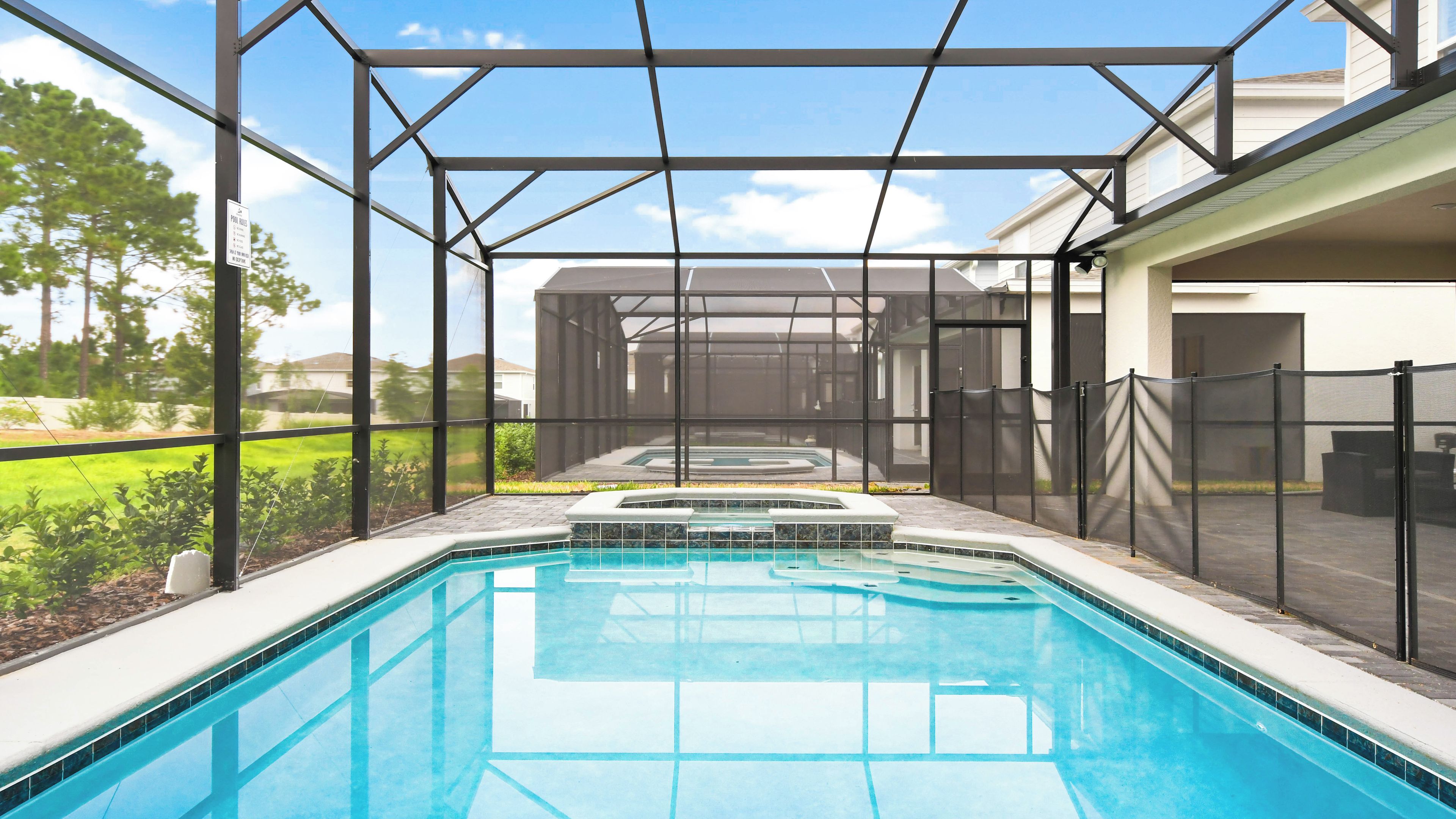 A swimming pool with a glass enclosure, a hot tub, and a view of a residential area.