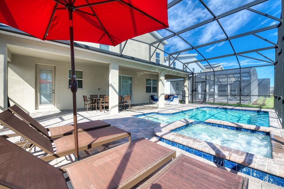 Un espace piscine avec des chaises longues et un parasol rouge, le tout abrité par une structure en verre.