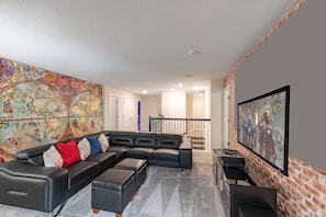 Ein Wohnzimmer mit Ecksofa, einer großformatigen Weltkarten-Wandmalerei, einem Flachbildfernseher und einer Ziegelwand als Blickfang.