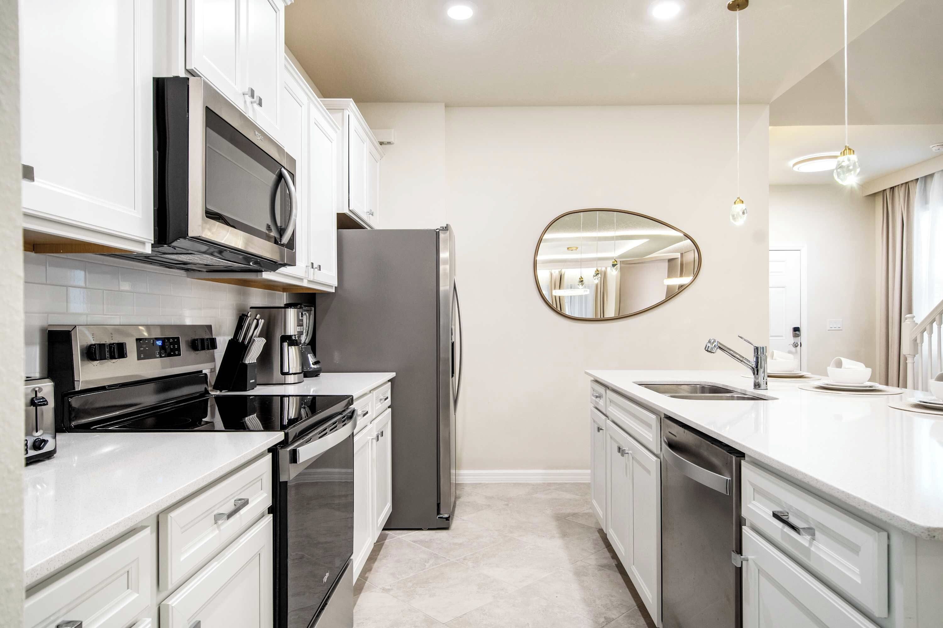 A modern kitchen with white cabinetry, stainless steel appliances, a large mirror, and a clean, tiled floor.