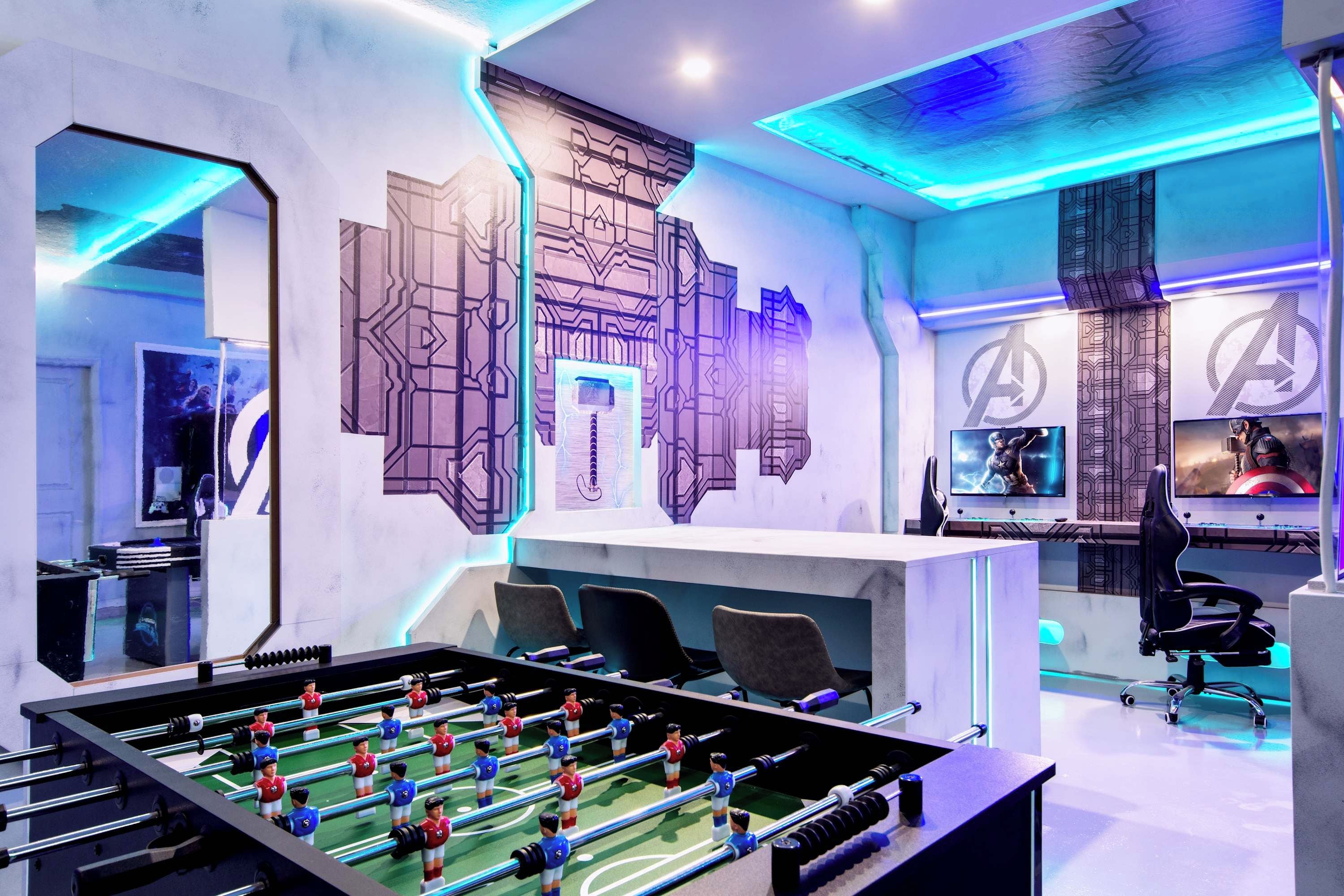 A modern room with a foosball table, multiple screens, and a unique geometric wall design.