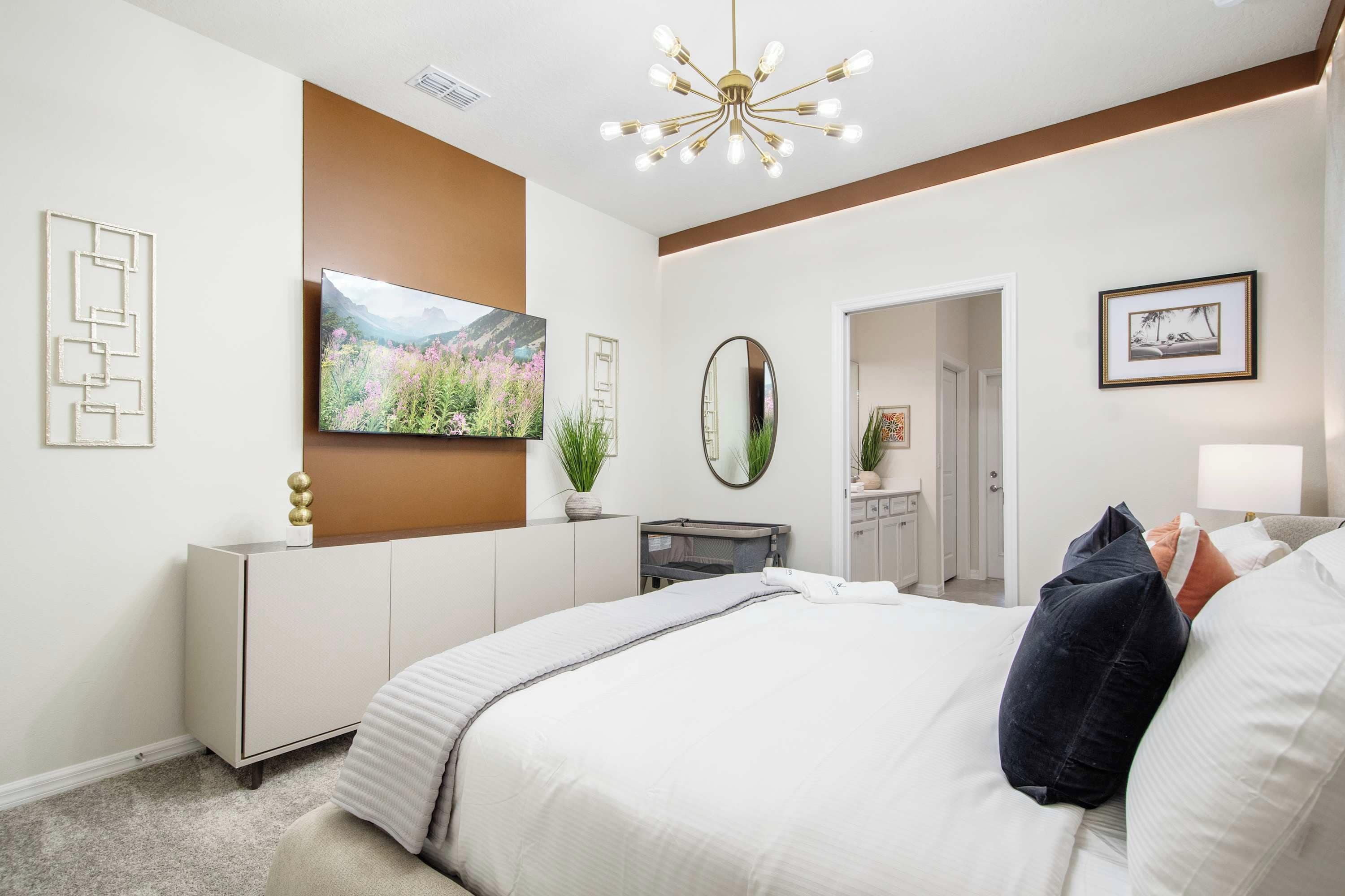A bedroom with a large bed, a television mounted on the wall, a mirror, and a door leading to a bathroom.