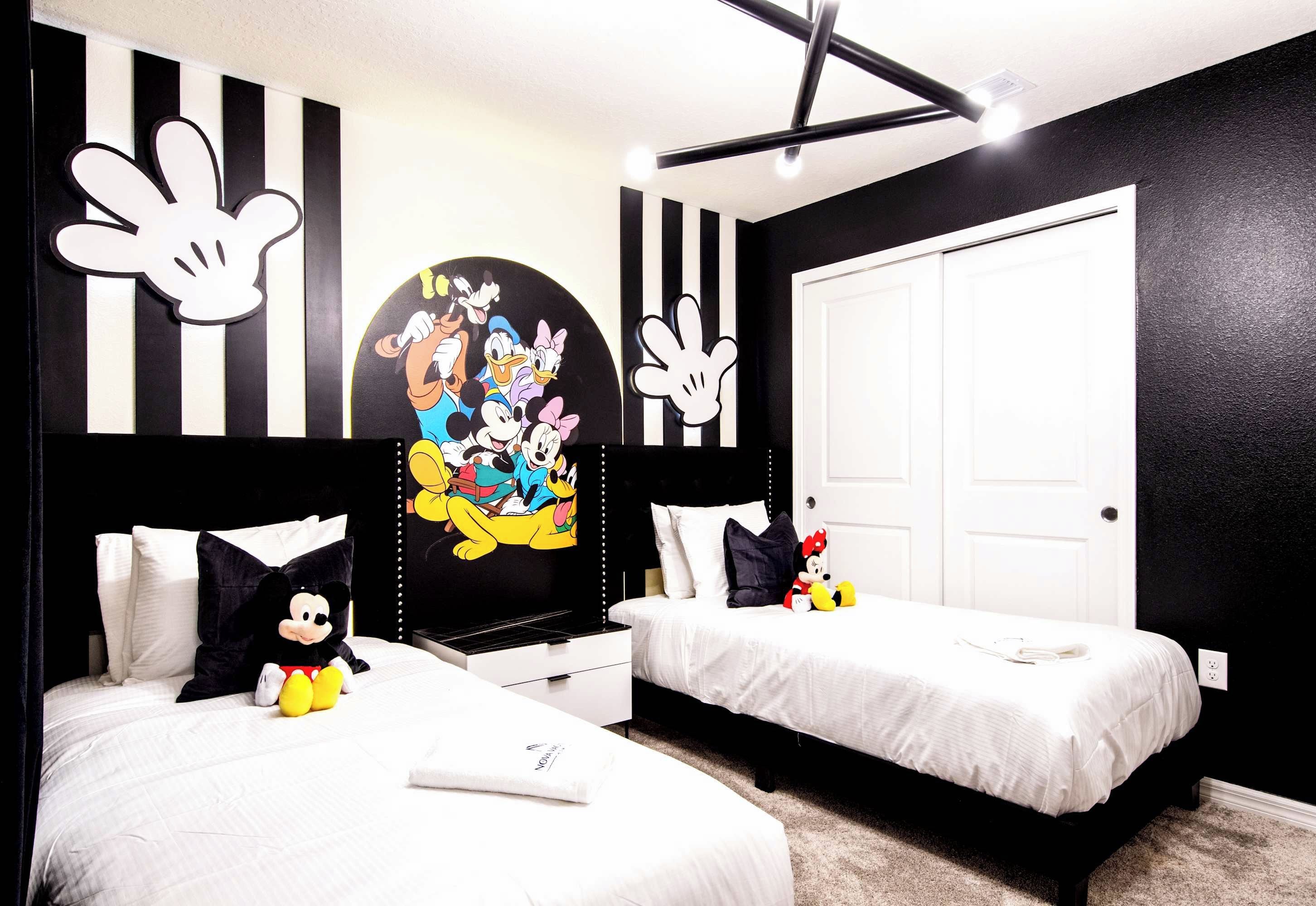 Habitación de hotel con dos camas, paredes a rayas blancas y negras, decoraci ón con personajes de Mickey Mouse y Disney, y una puerta blanca.