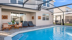 A swimming pool with lounge chairs and a table, surrounded by a covered patio area. - Star Wars & Frozen Bunks, Pool, Game Room/disney! (Davenport)
