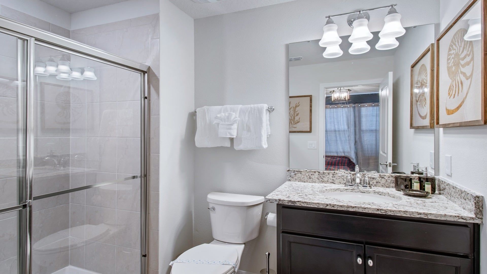Une salle de bain moderne avec une douche à parois de verre, des toilettes blanches, un meuble-lavabo avec un plan de travail en marbre et un miroir agrémenté de luminaires fixés au mur.