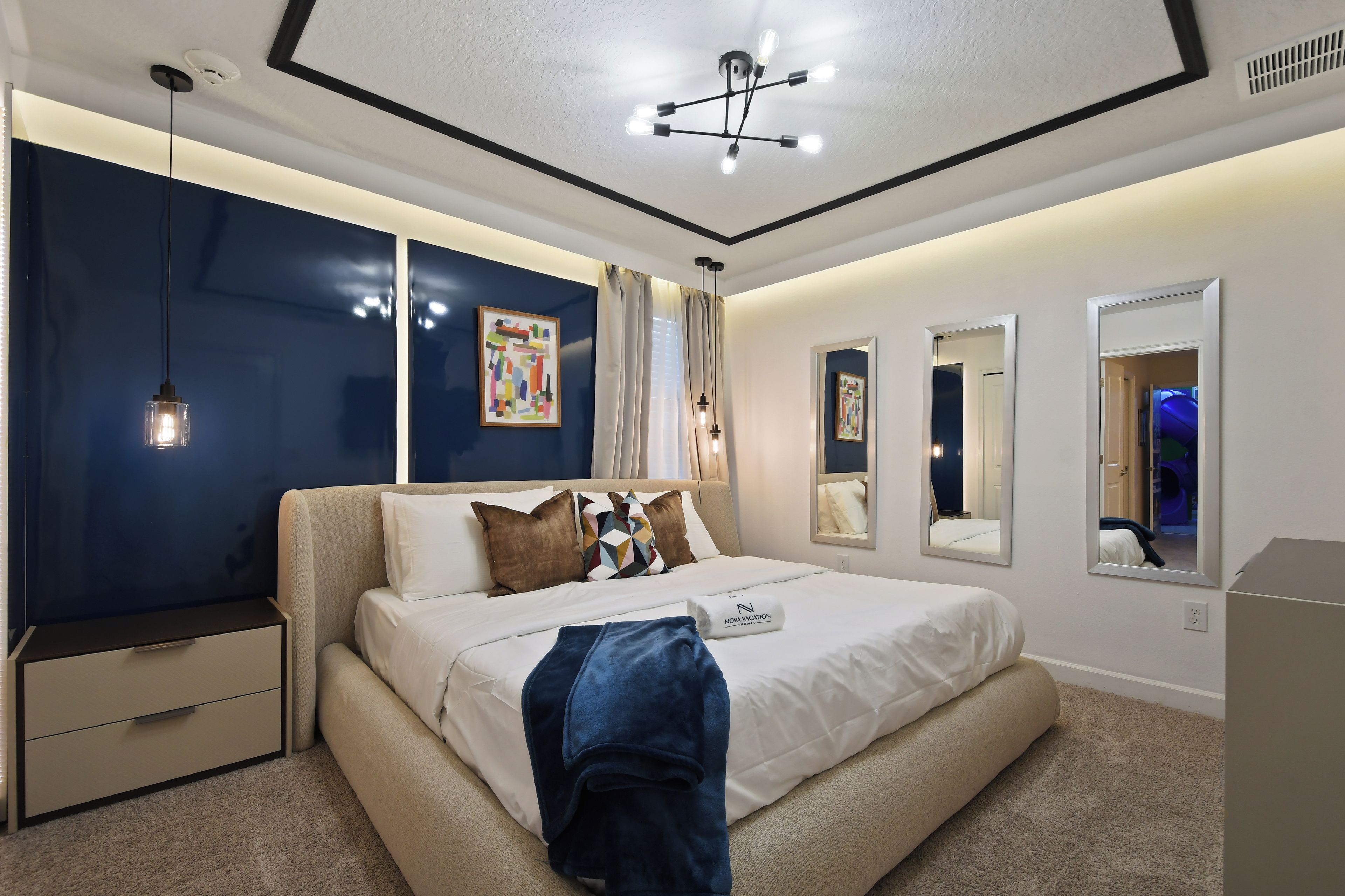 Un dormitorio moderno con una cama, mesitas de noche, una lámpara de techo y obras de arte en las paredes.
