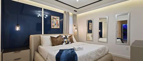 Une chambre à coucher moderne, avec un lit, des tables de chevet, un luminaire au plafond et des œuvres d’art accrochées aux murs.