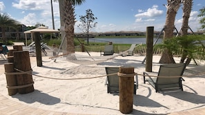 A sandy outdoor area with a hammock, chairs, and a view of a body of water. - Lakeview Home w/ Mario Game Room & Themed Bedrooms (Kissimmee)