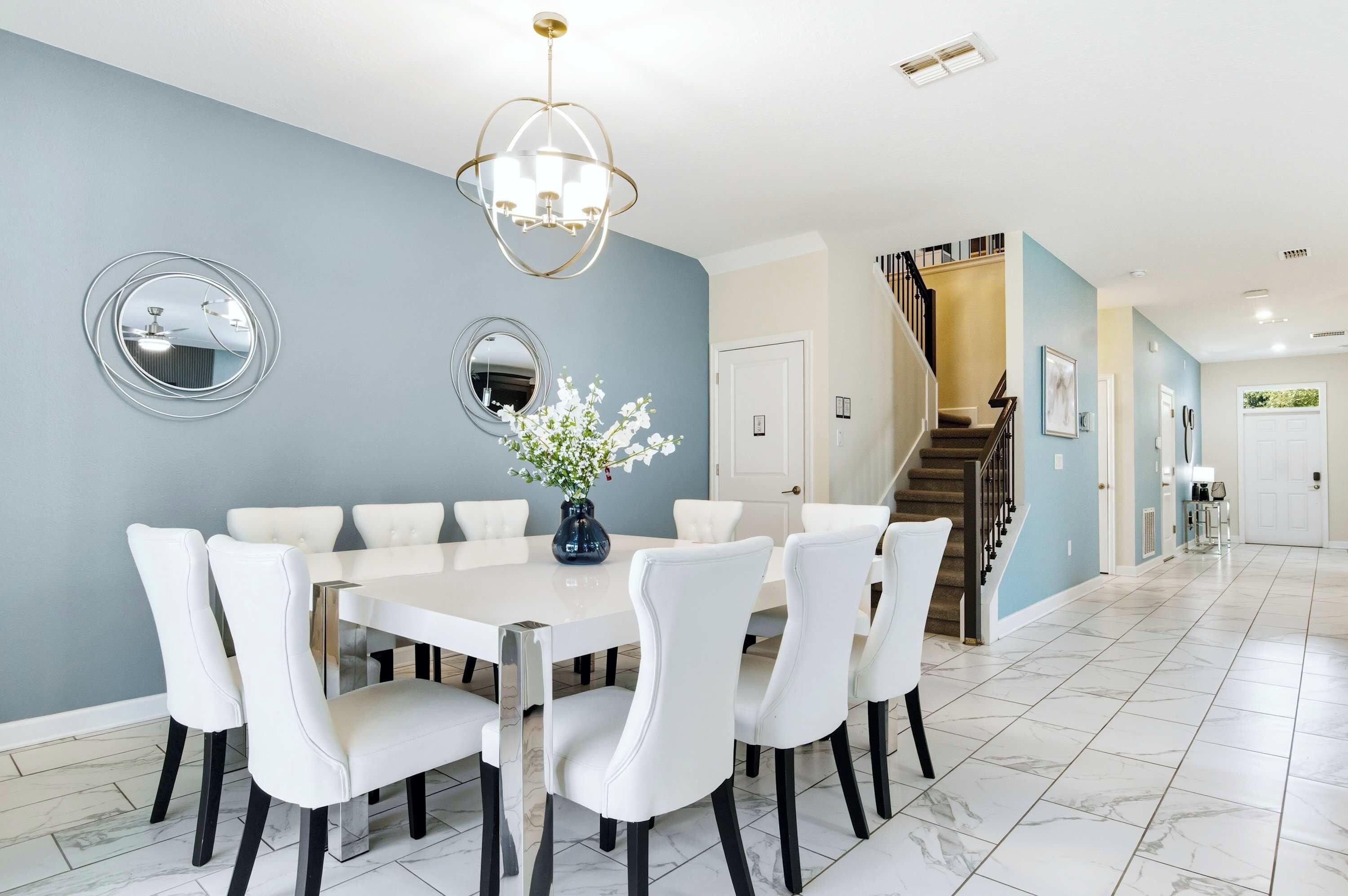 A dining area with a white table and chairs, a chandelier, and a vase with flowers.