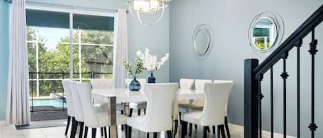 A dining area with a table and chairs, a chandelier, and a view of a swimming pool.