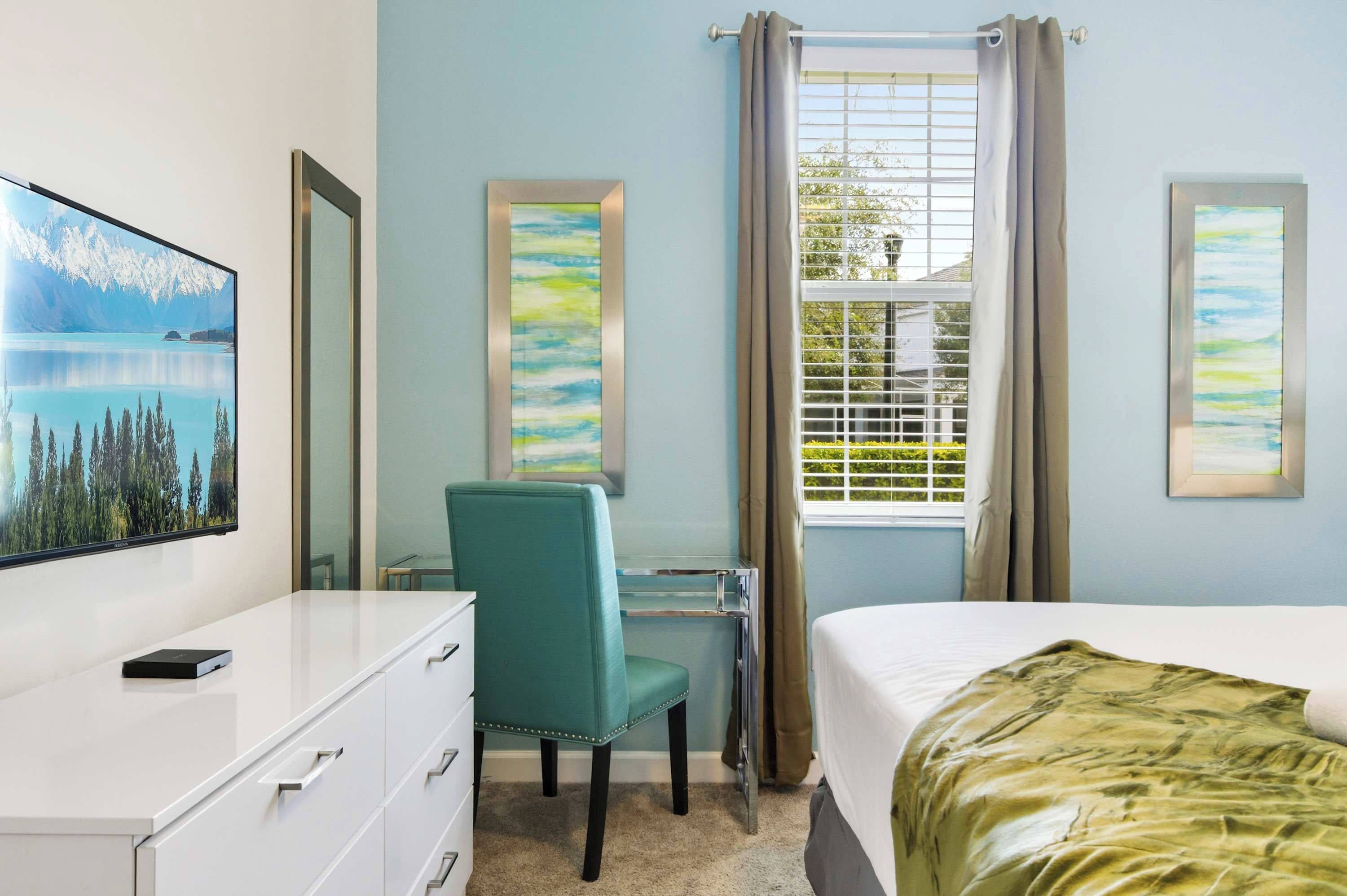 A hotel room with a bed, a desk with a chair, a dresser, and a window with curtains.