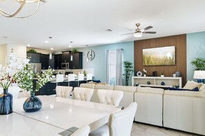 Ein modernes Wohnzimmer mit einem weißen Sofa, einem Esstisch mit Stühlen und einer Küche im Hintergrund.