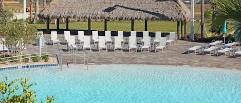 A swimming pool with lounge chairs and a thatched-roof structure.