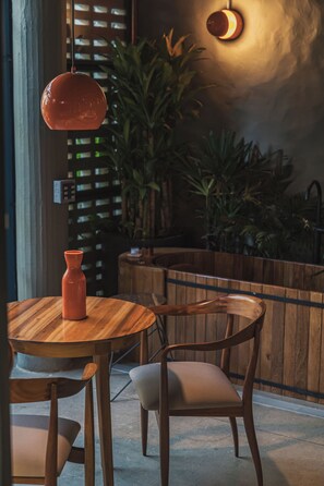 Una mesa de madera con un florero, una silla y una lámpara colgante en una habitación con plantas y una encimera de madera.