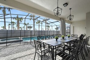 A covered outdoor patio with a pool, a dining table with chairs, and hanging lights. - Family Fun Villa: Themed Rooms, Private Pool & Spa (Clermont)