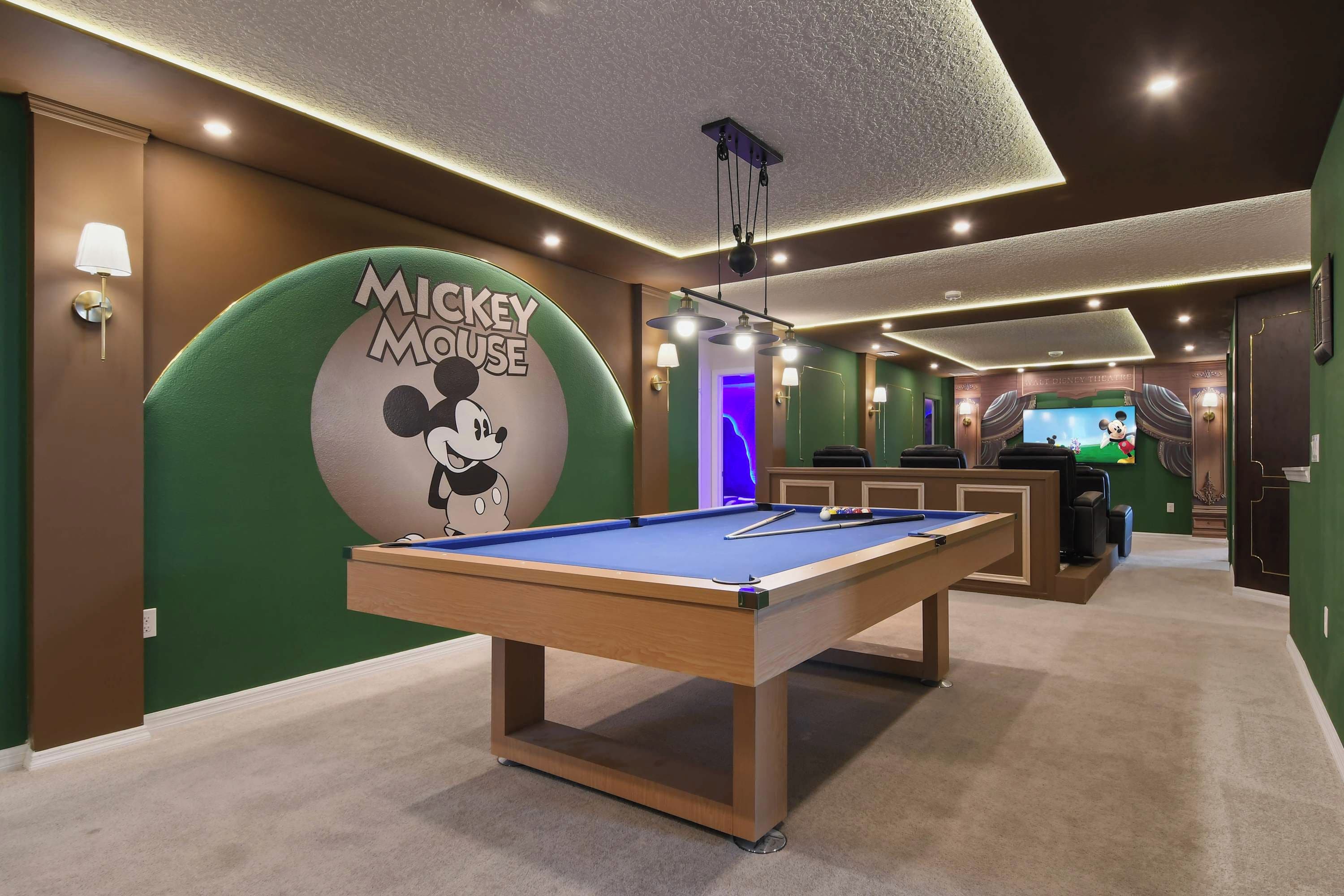 A pool table in a room with a Mickey Mouse mural, a TV, and a bar area.